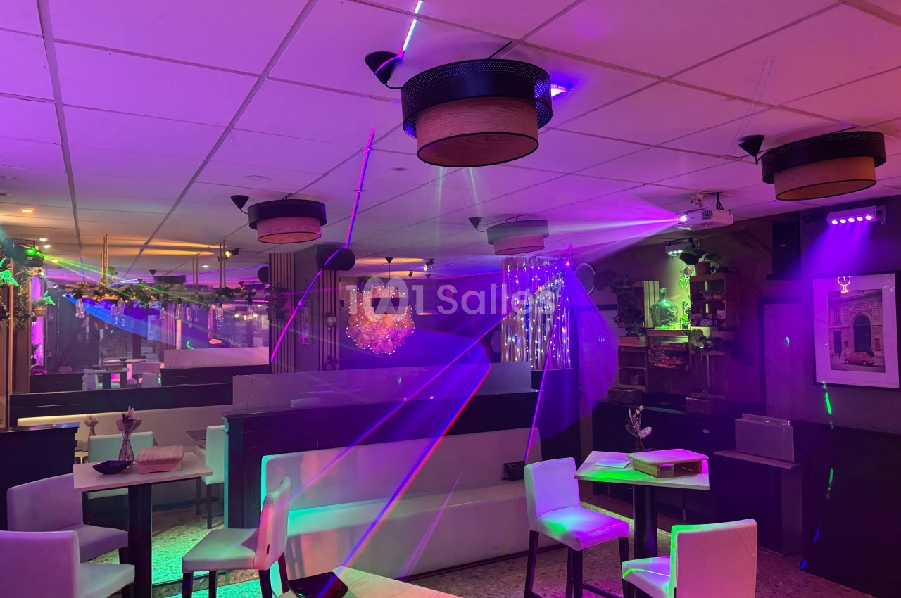 Salle de restaurant avec éclairage tamisé et jeux de lumière colorés, tables et chaises disposées pour des convives.