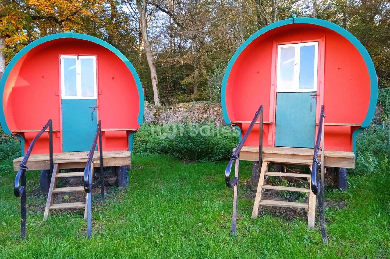 Deux roulottes rouges avec portes vertes, posées sur un terrain herbeux devant des arbres en automne.
