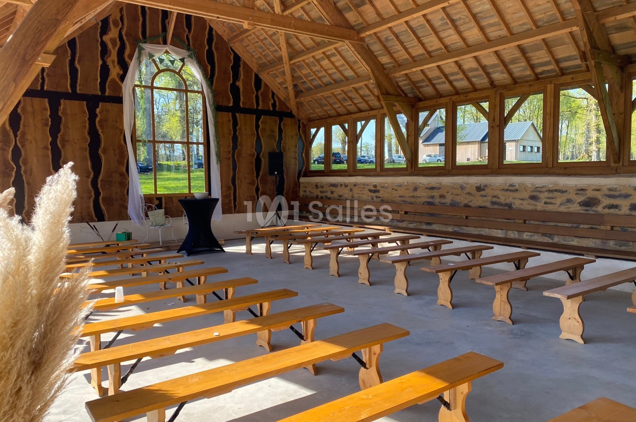 Salle en bois avec bancs alignés, grandes fenêtres laissant entrer la lumière et vue sur l'extérieur verdoyant.