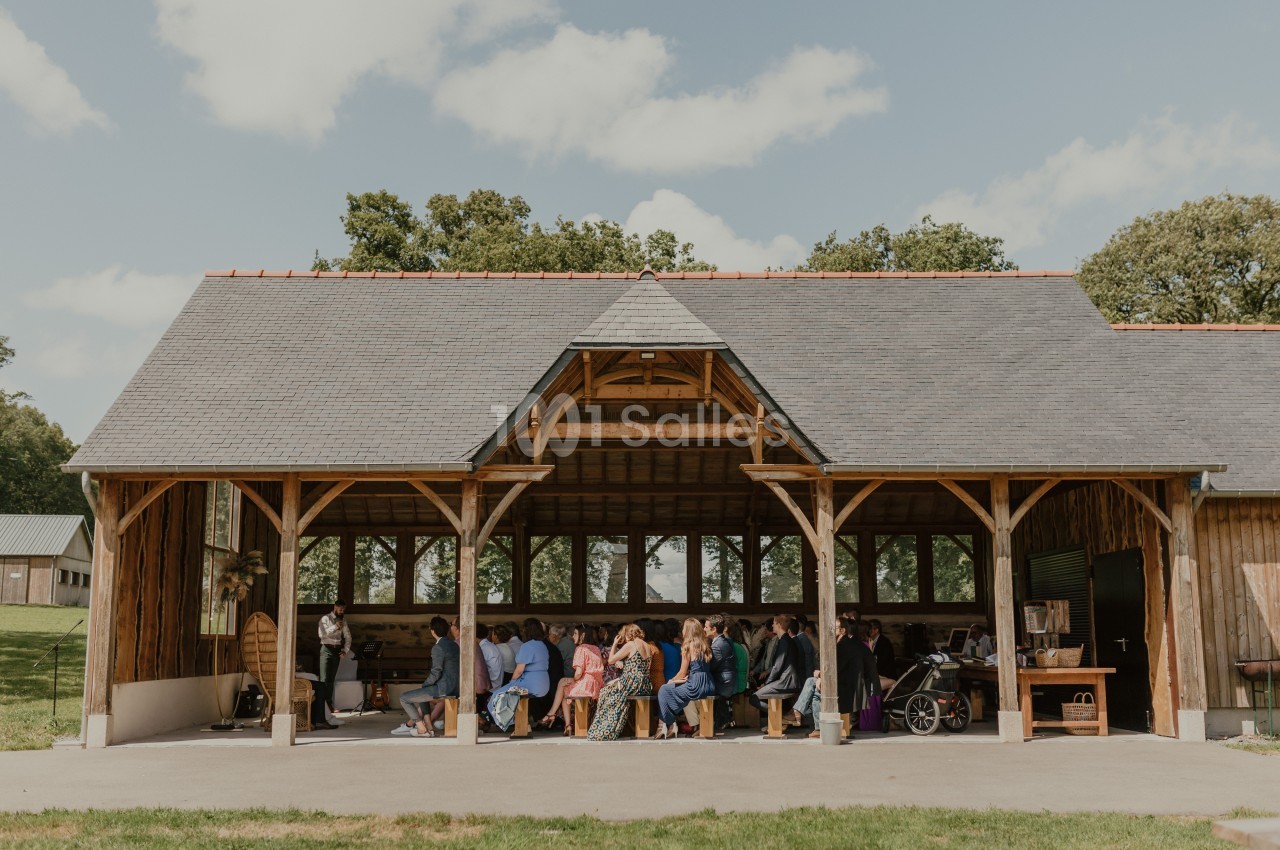 Un groupe de personnes assises sous un grand abri en bois ouvert, entouré de verdure et de ciel dégagé.