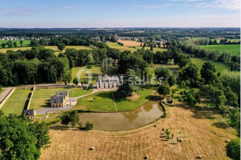 Vue aérienne d'un domaine avec un château, une chapelle, un étang et des champs entourés de verdure.