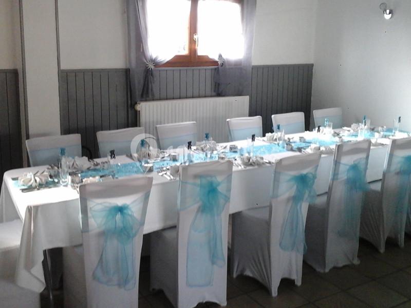 Table dressée pour un événement, avec nappes blanches, décorations bleues et chaises couvertes de housses assorties.