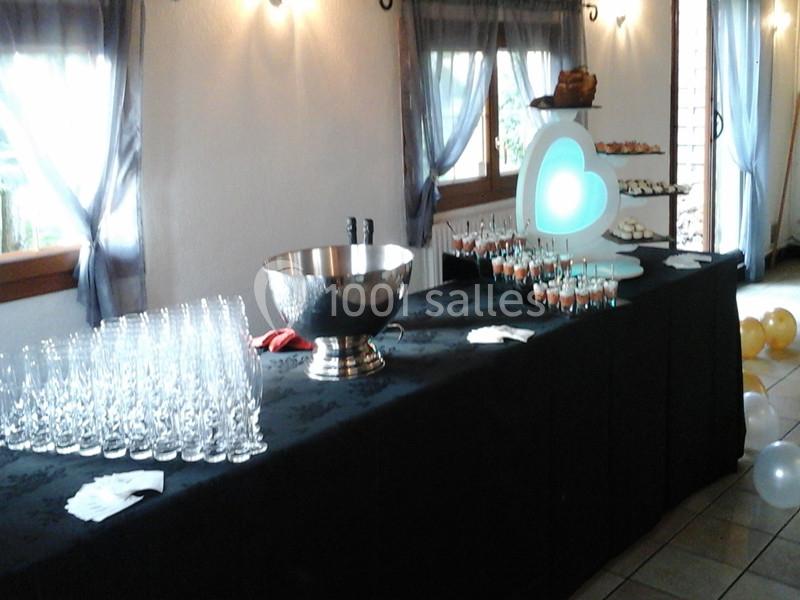 Table de réception avec verres, coupe en métal, desserts et décor lumineux en forme de cœur, dans une salle éclairée.