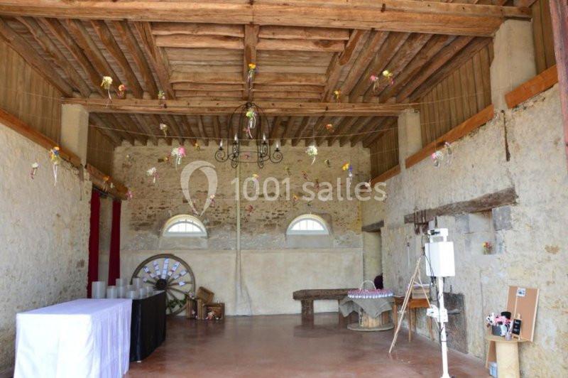 Intérieur d'une salle en pierre avec poutres apparentes, décorée de fleurs suspendues et équipée de tables.