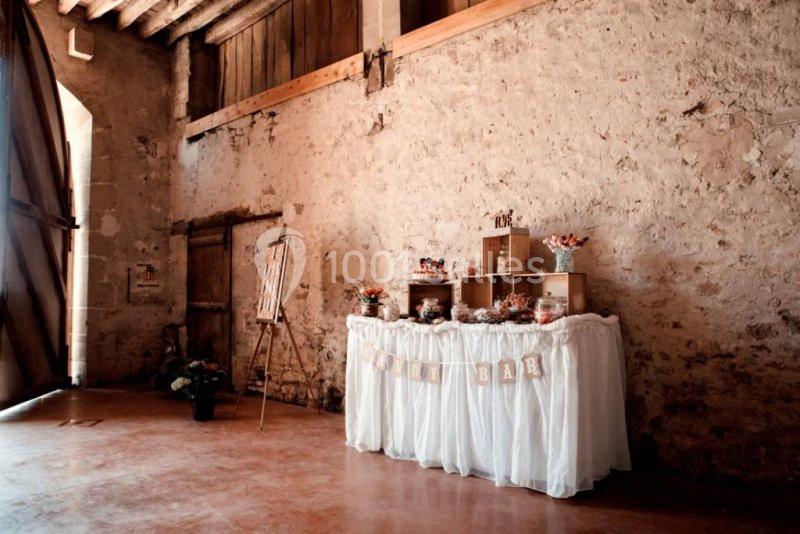 Table décorée pour un candy bar dans une grange en pierre, avec des bonbonnières et une guirlande en tissu.