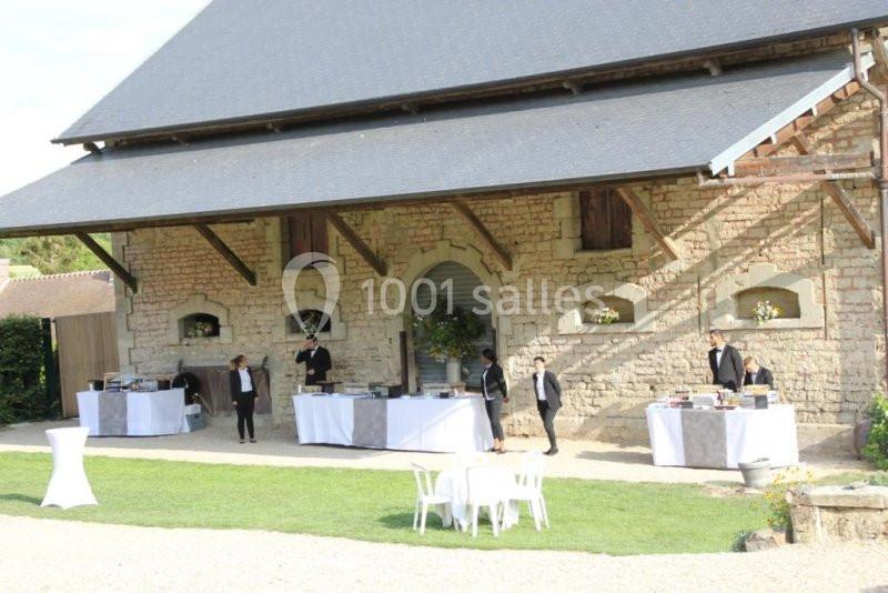 Un bâtiment en pierre avec des tables de buffet installées à l'extérieur et des serveurs en tenue formelle.