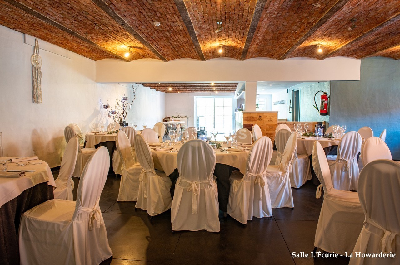 Salle de réception avec tables dressées, chaises couvertes de housses blanches et plafond voûté en briques.