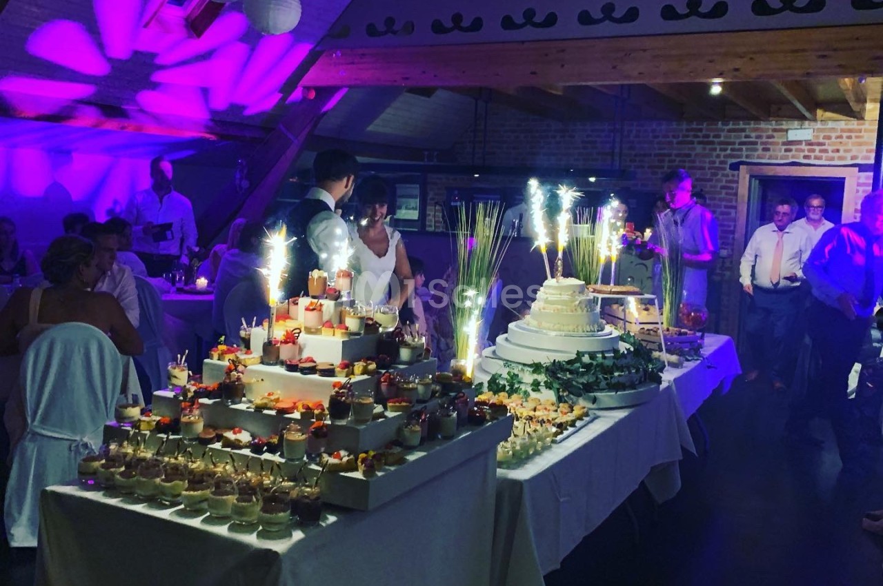 Table de desserts variés avec gâteaux, verrines et décorations lumineuses dans une salle de réception festive.