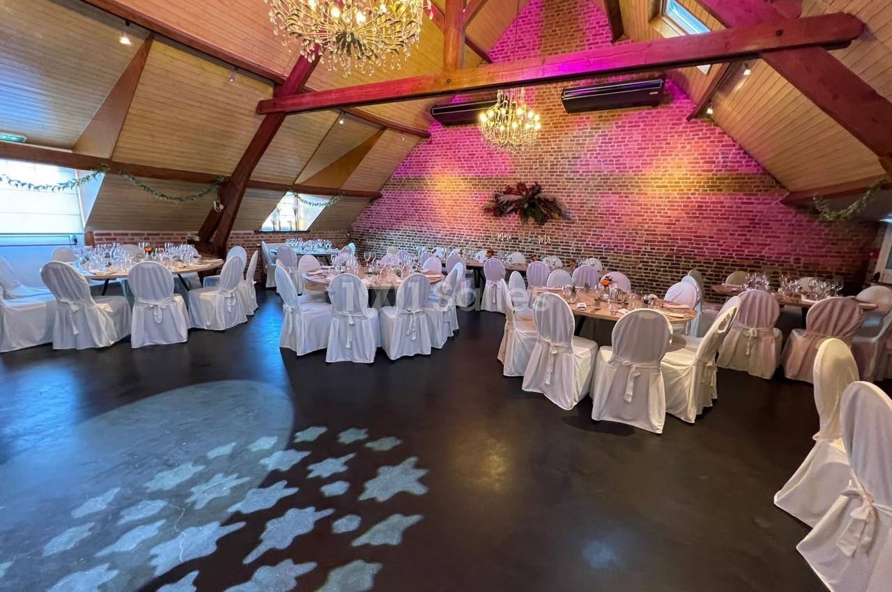 Salle de réception décorée avec des tables dressées, des chaises blanches et des lustres suspendus sous un plafond en bois.
