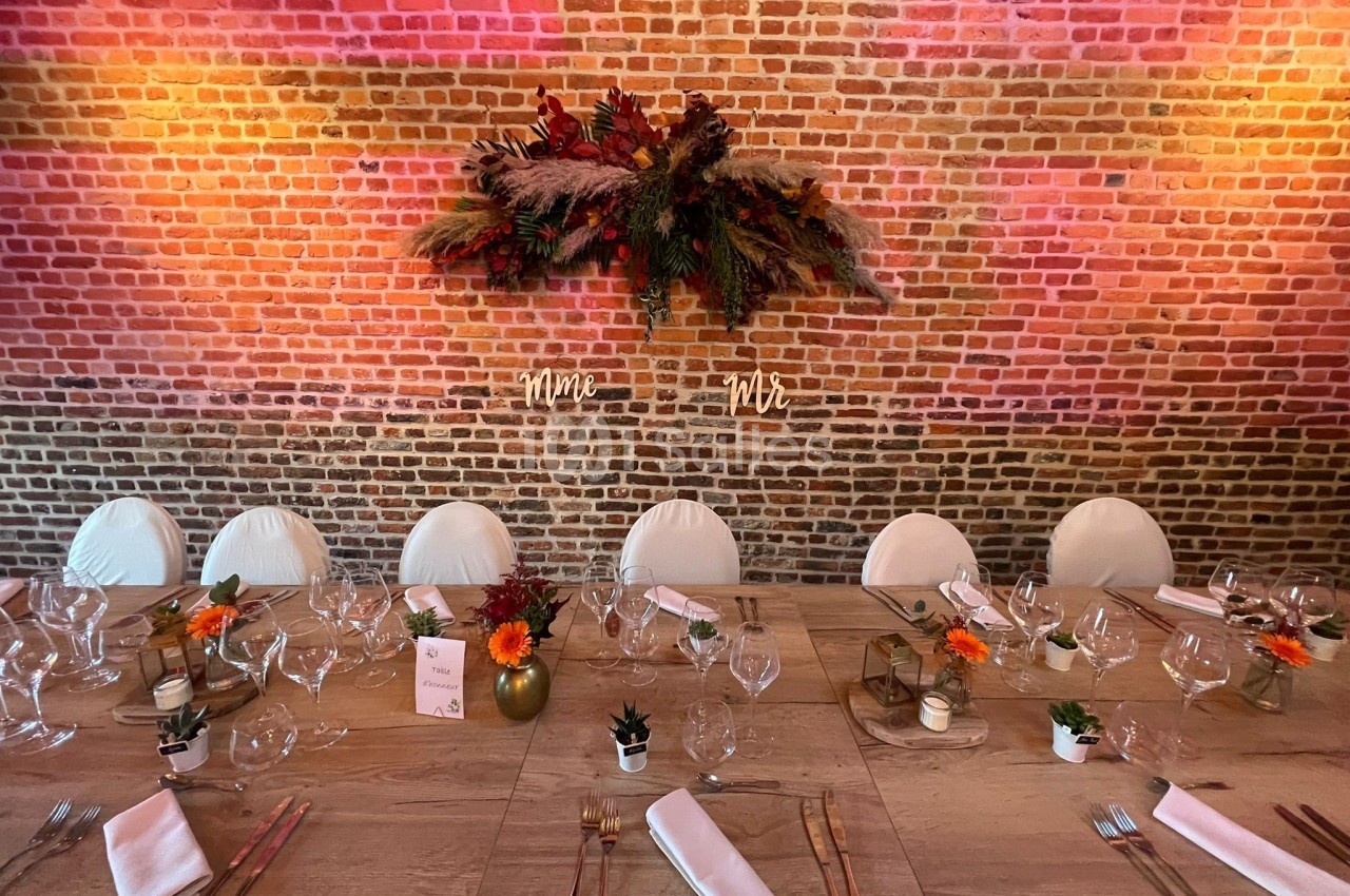 Table décorée pour un repas festif avec vaisselle élégante, fleurs colorées et mur de briques en arrière-plan.