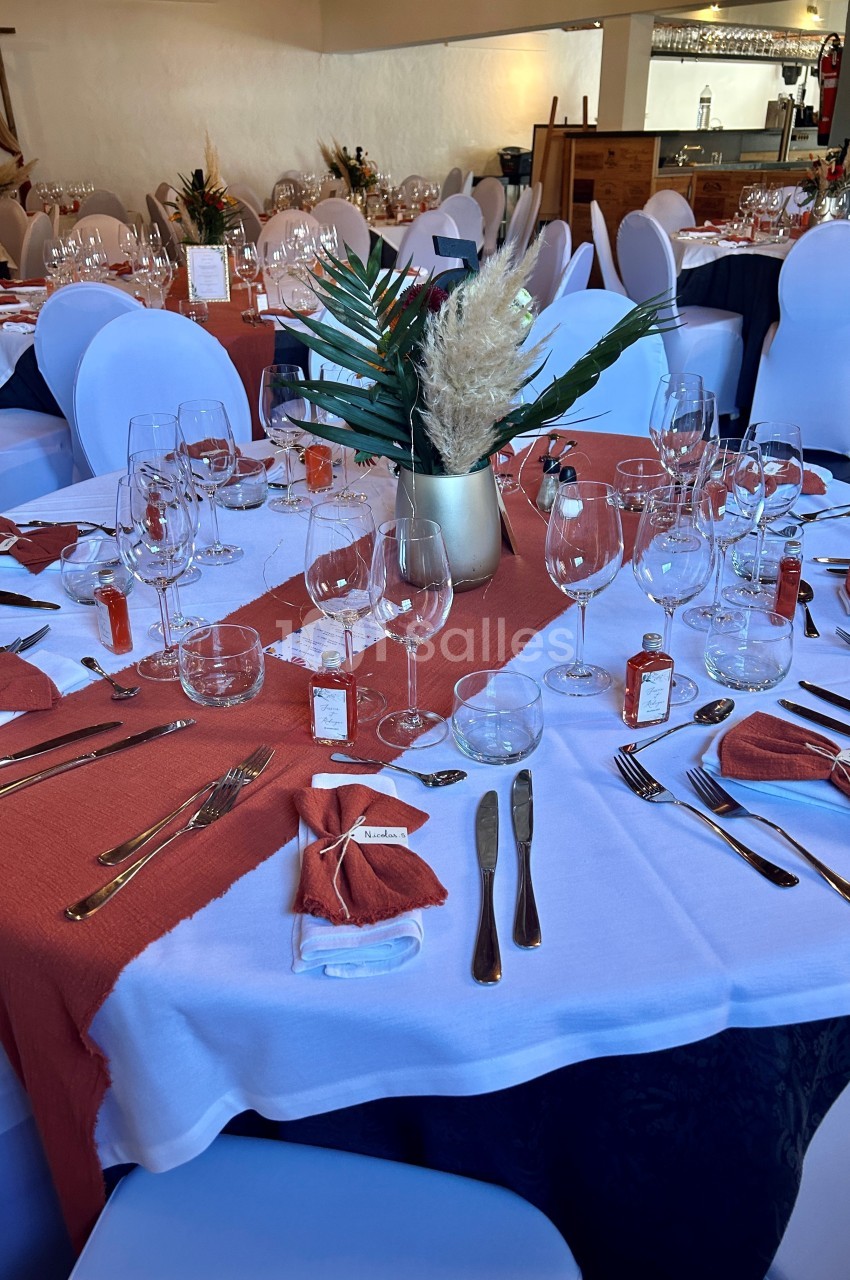 Table de réception élégamment dressée avec nappes blanches, chemins de table rouges, couverts et verres disposés.