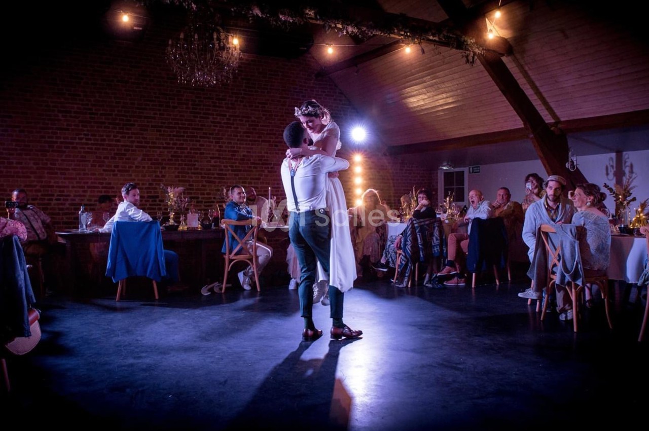 Un couple danse au centre d'une salle éclairée, entouré d'invités assis à des tables.