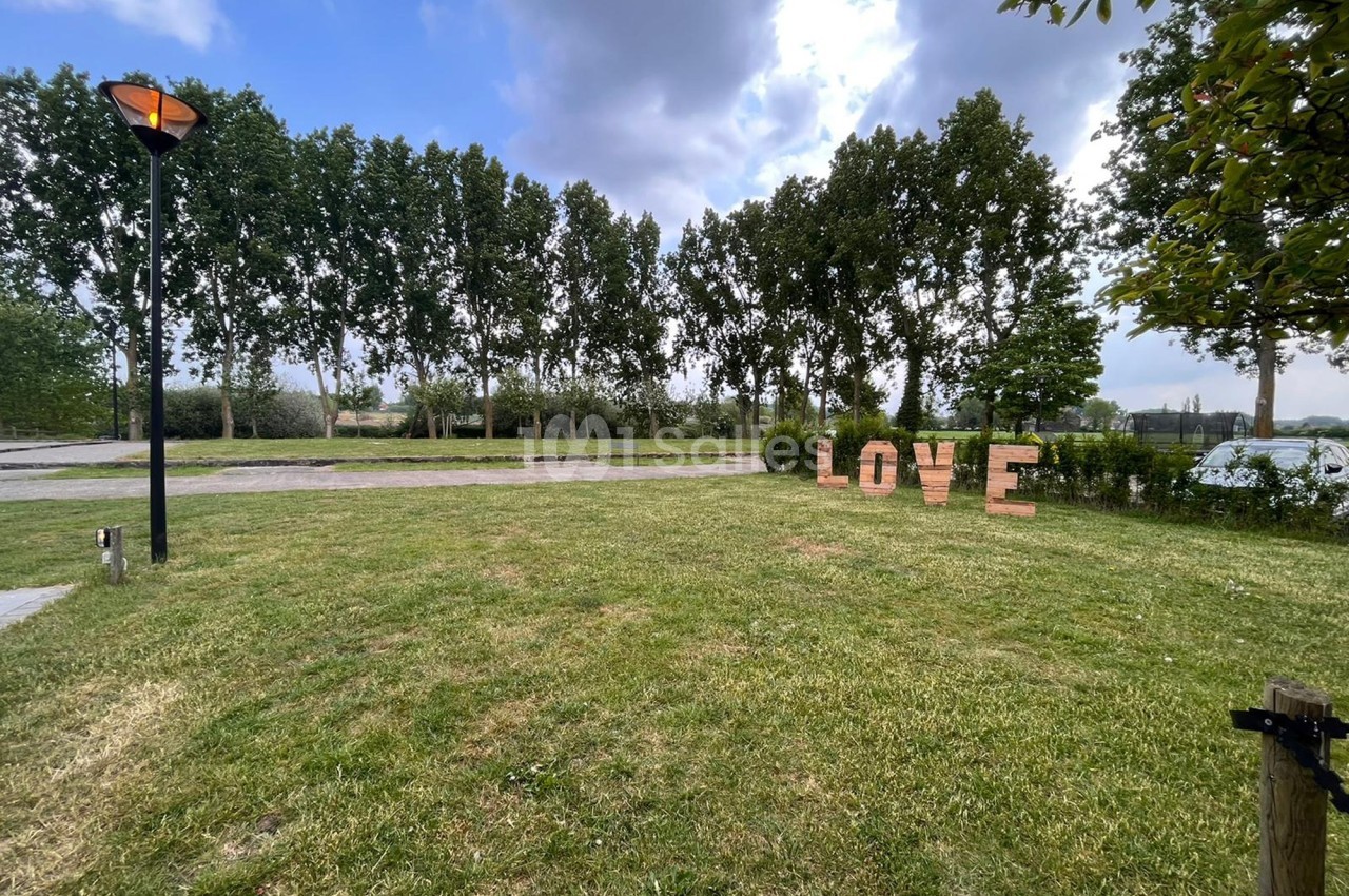 Pelouse avec des lettres formant le mot ’LOVE’, alignées près d'une route bordée d'arbres sous un ciel partiellement nuageux.