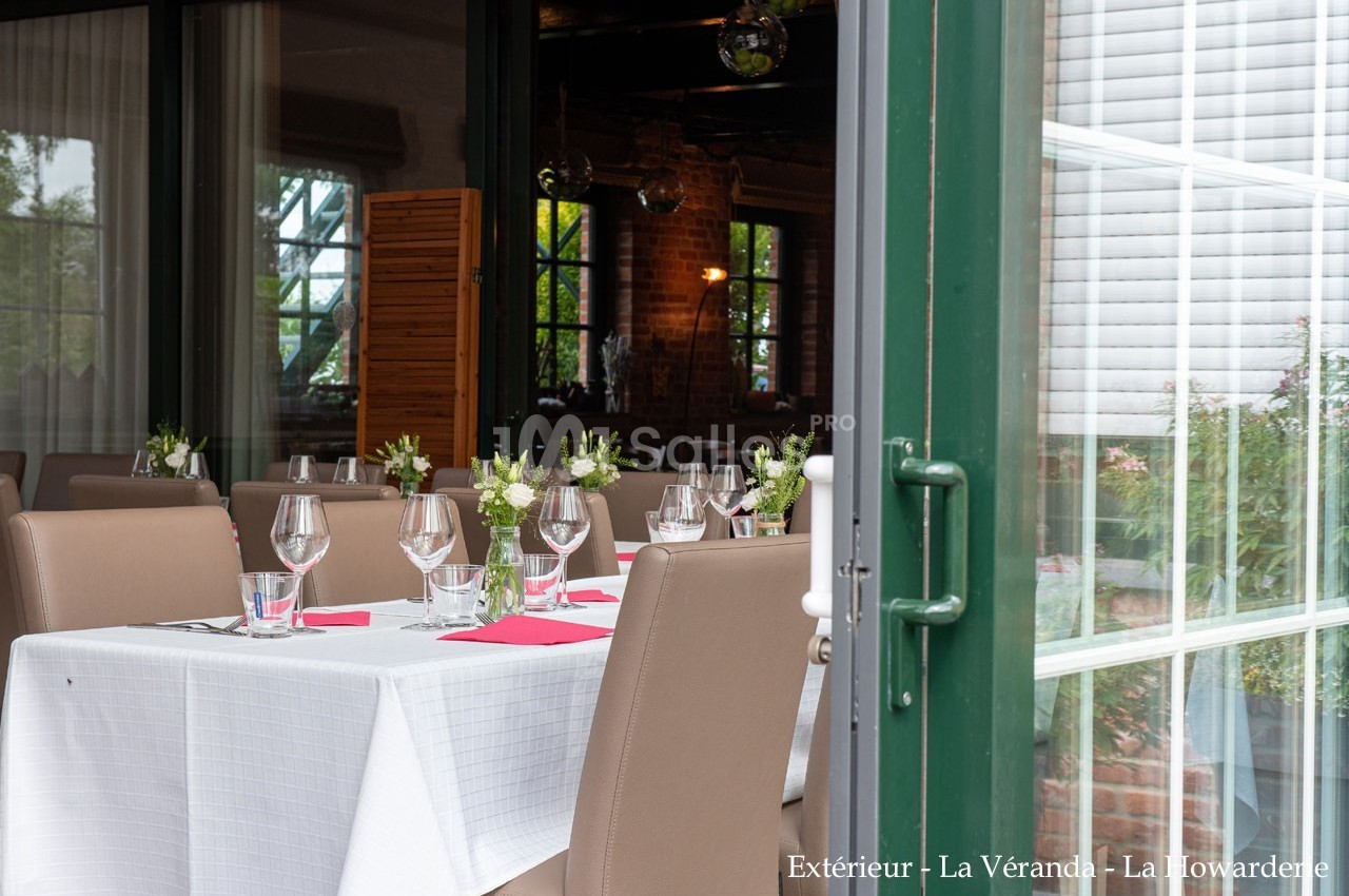 Table dressée avec nappes blanches, verres et fleurs, située près d'une baie vitrée ouverte donnant sur un espace verdoyant.