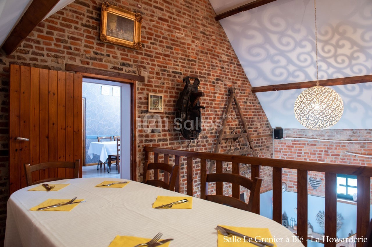 Salle à manger avec murs en briques, table dressée avec nappes jaunes et vue sur une pièce adjacente.