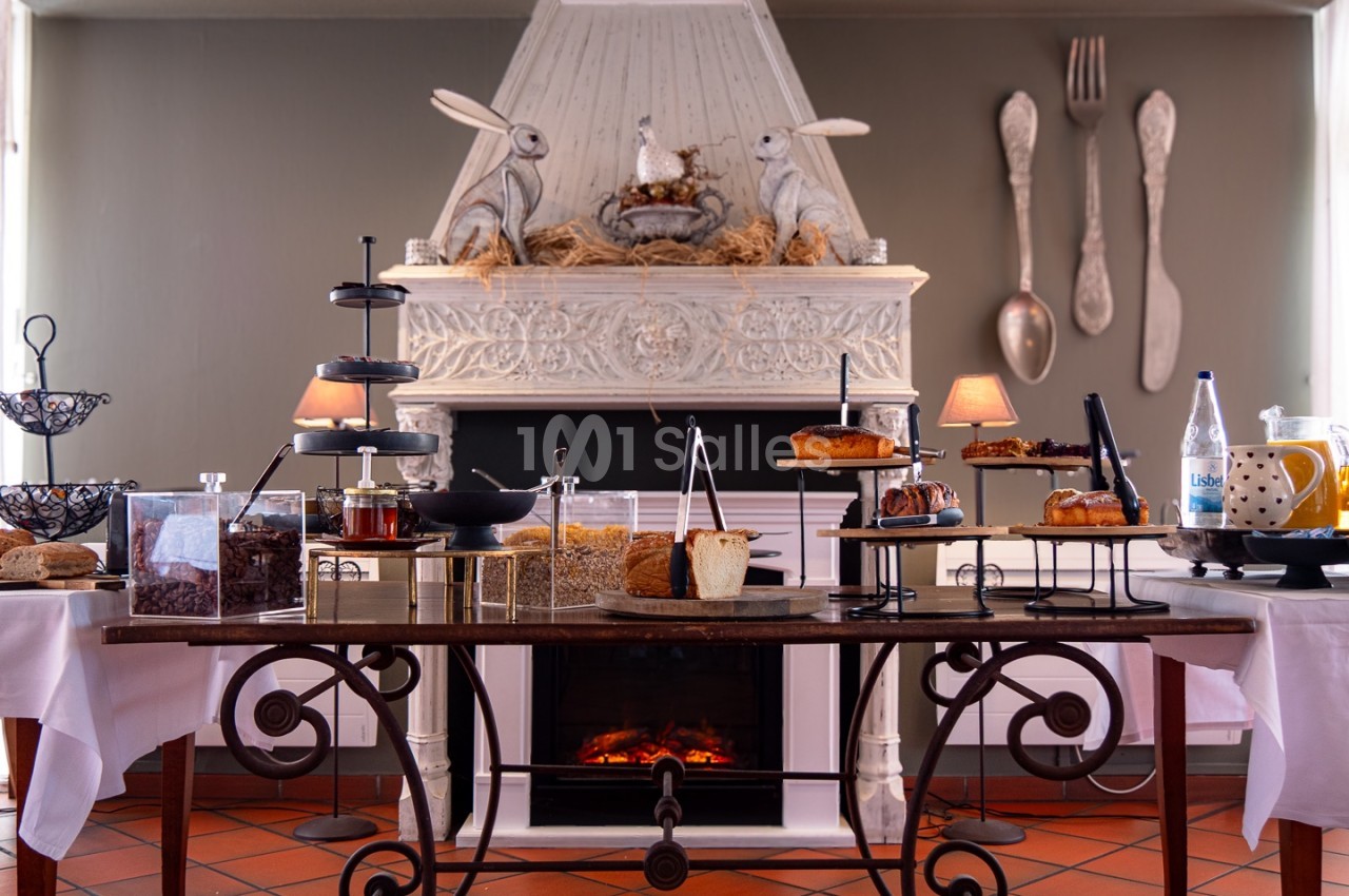 Table garnie de desserts variés devant une cheminée décorée avec des lapins et des ustensiles géants accrochés au mur.