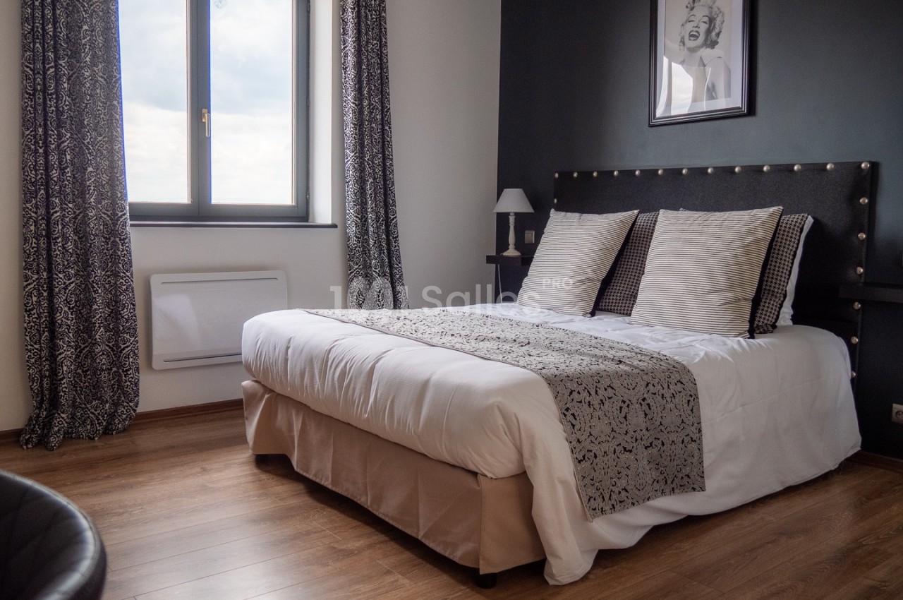 Chambre avec lit double, parquet, rideaux à motifs, mur sombre et fenêtre laissant entrer la lumière naturelle.