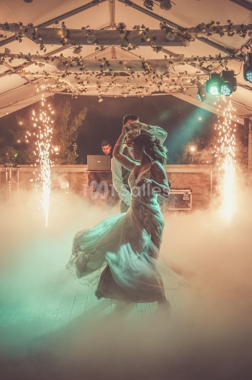 Un couple danse sous une tente décorée, entouré de fumée et d'effets lumineux avec des étincelles en arrière-plan.