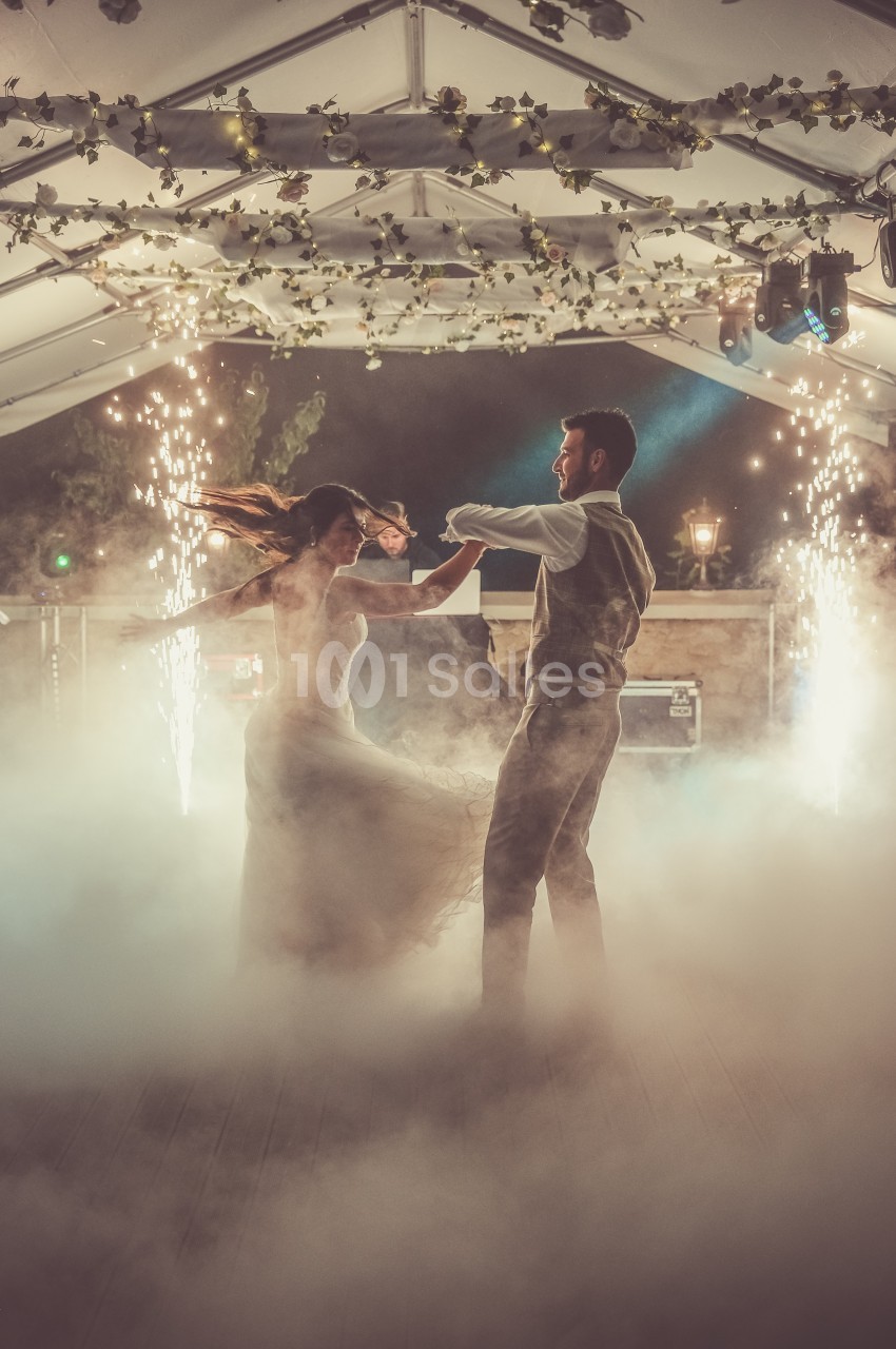 Un couple danse sous une tente décorée, entouré de fumée et d'étincelles dans une ambiance festive.