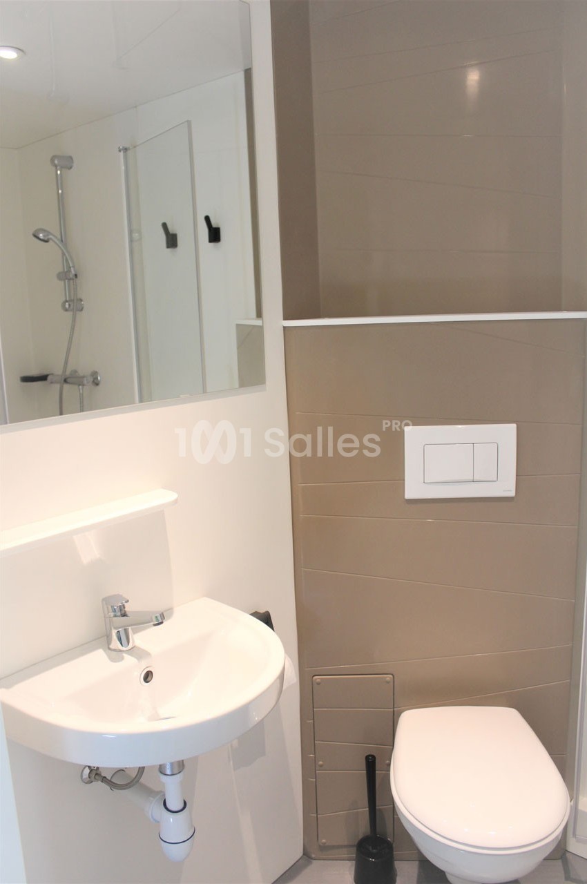 Salle de bain moderne avec lavabo, miroir, toilettes suspendues et douche en arrière-plan.