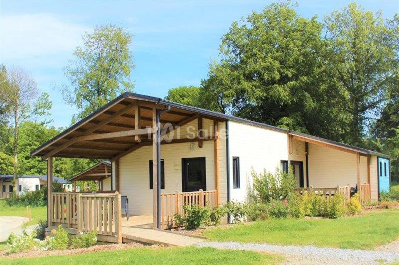 Chalet en bois clair avec terrasse couverte, entouré de verdure et situé dans un environnement arboré.