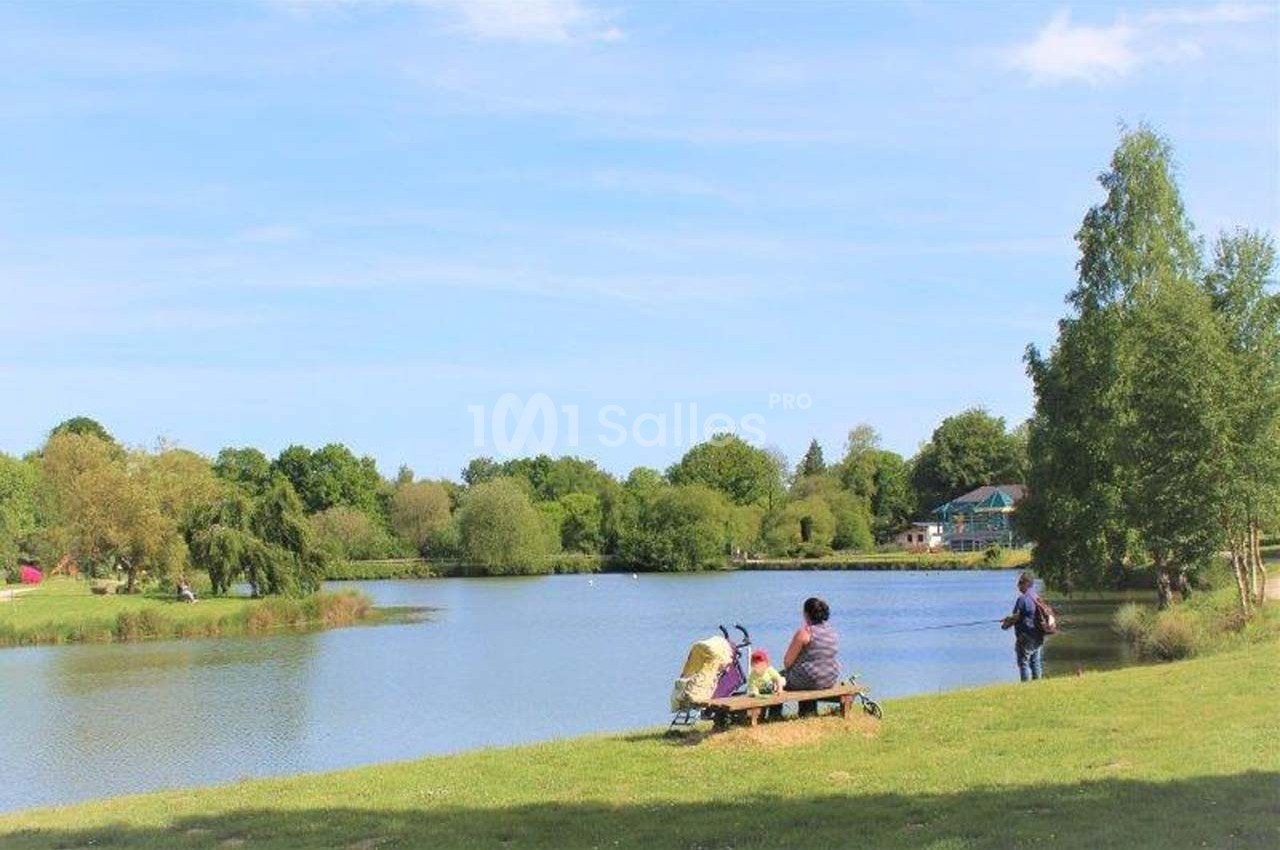 Deux personnes assises sur un banc près d'un lac entouré d'arbres, sous un ciel dégagé.