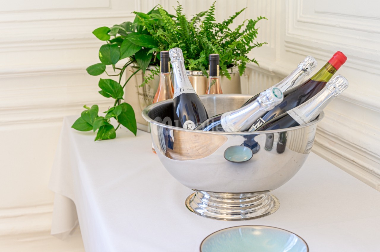 Des bouteilles de vin et de champagne dans un seau en métal, posées sur une table avec des plantes en arrière-plan.