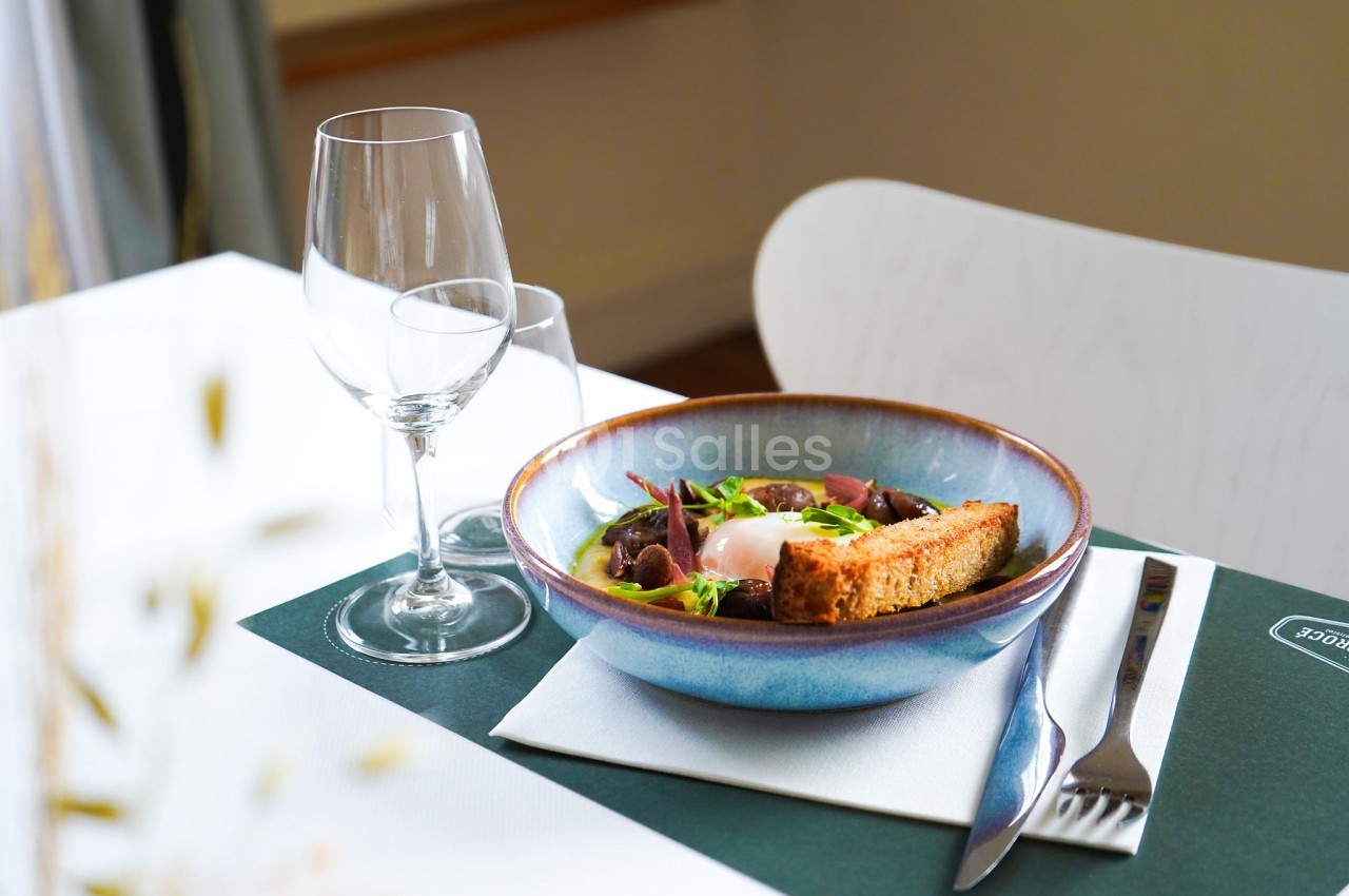 Assiette contenant un œuf poché, des légumes et du pain grillé, posée sur une table avec des verres et des couverts.