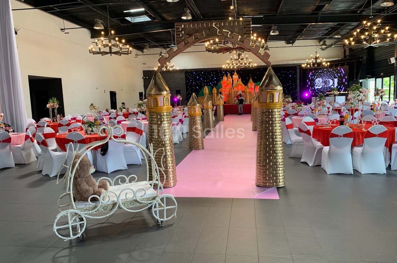 Salle de réception décorée avec des tables dressées, une arche dorée en forme de château et un carrosse miniature.