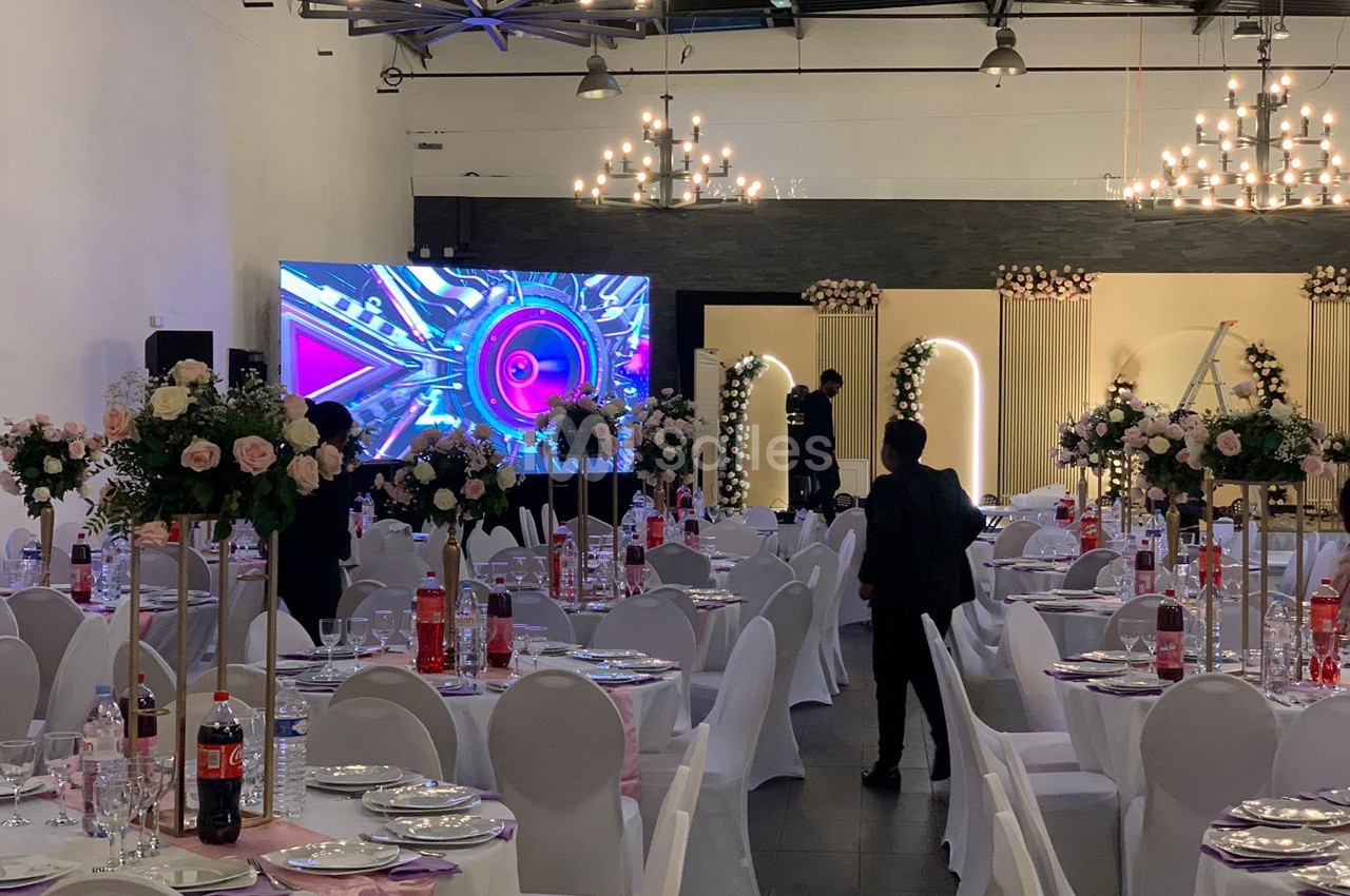 Salle de réception décorée avec des tables dressées, des fleurs et un écran géant affichant des graphismes colorés.