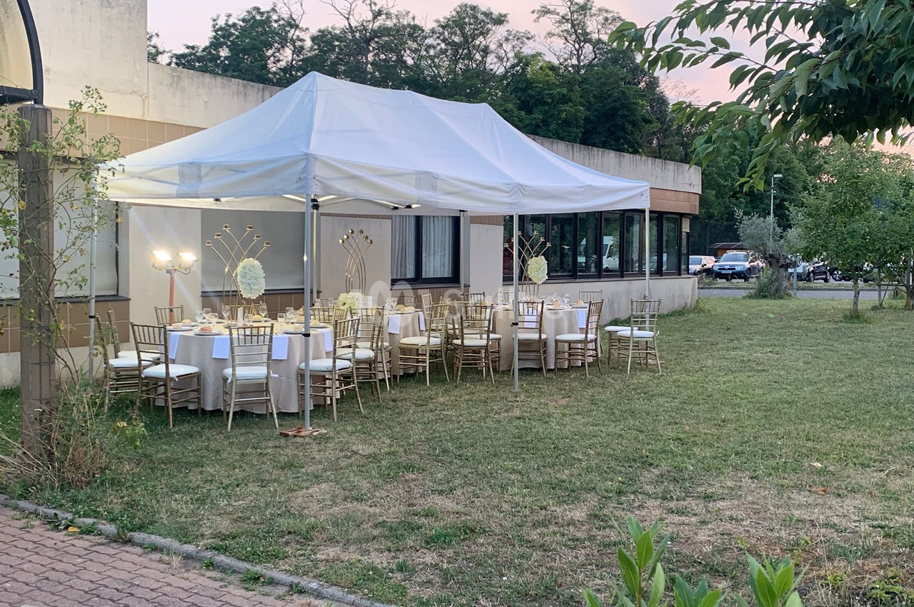 Tente blanche installée dans un jardin, abritant des tables décorées pour un événement en extérieur.