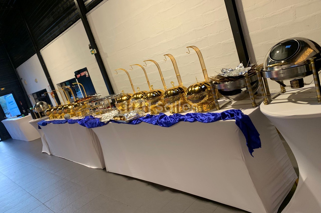Buffet avec plats chauds présentés dans des récipients dorés et argentés sur des tables recouvertes de nappes blanches.