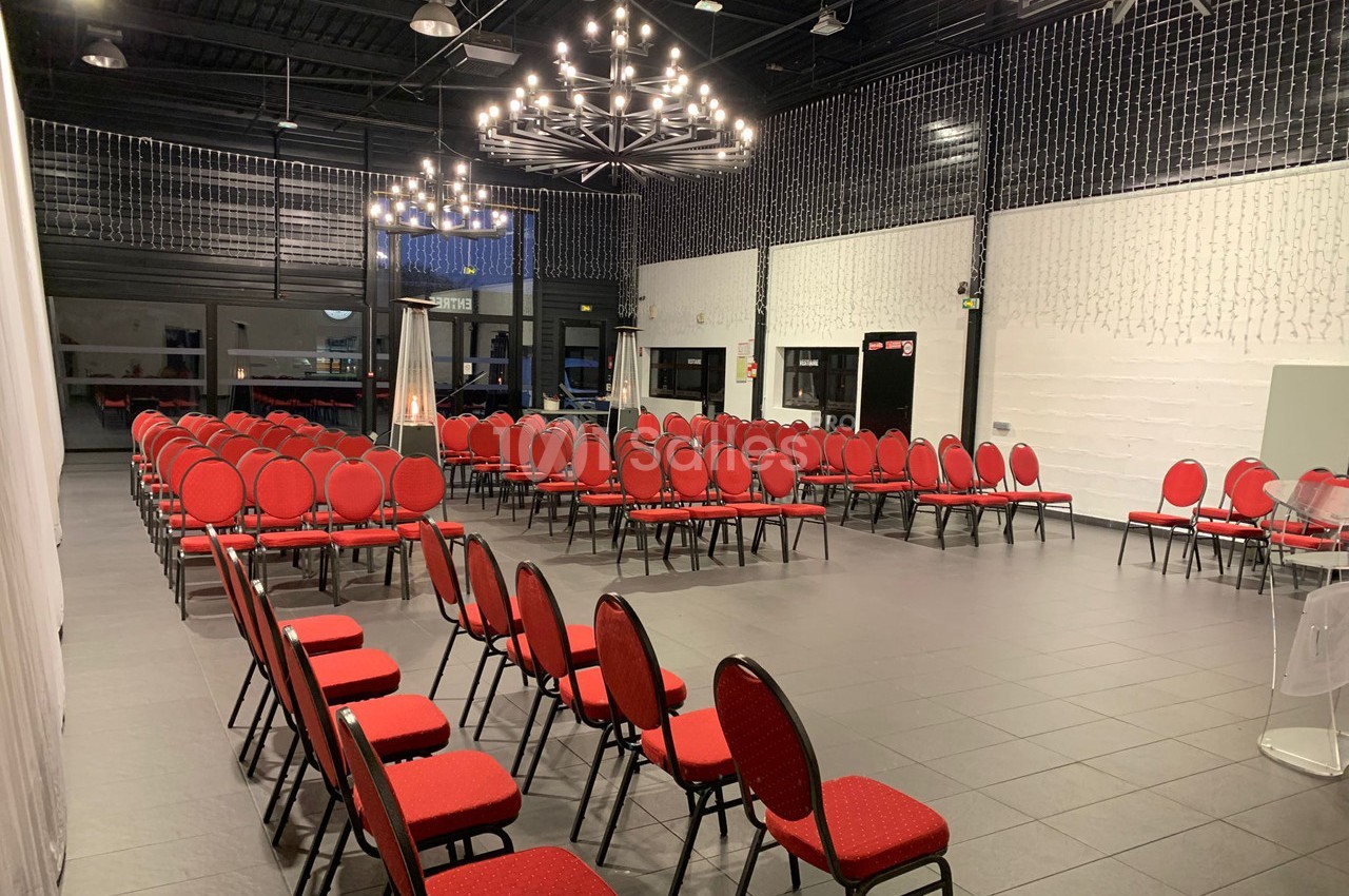 Salle de réception avec chaises rouges alignées, éclairée par des lustres modernes et des guirlandes lumineuses.