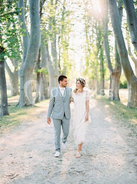 Un couple marche main dans la main sur un chemin bordé d'arbres, baigné par une lumière douce.