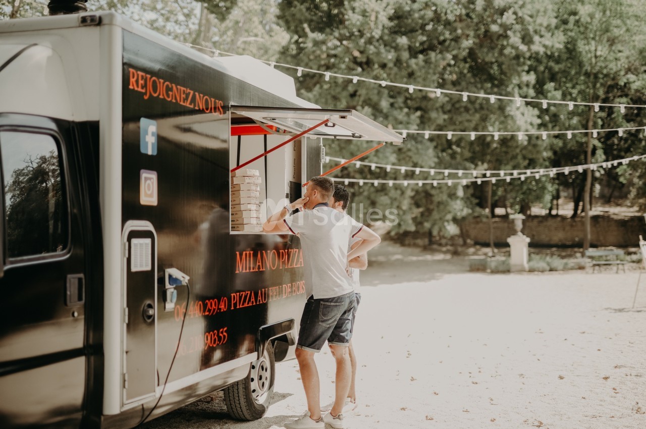 Deux personnes commandent à un food truck noir stationné en extérieur, entouré d'arbres et de guirlandes lumineuses.