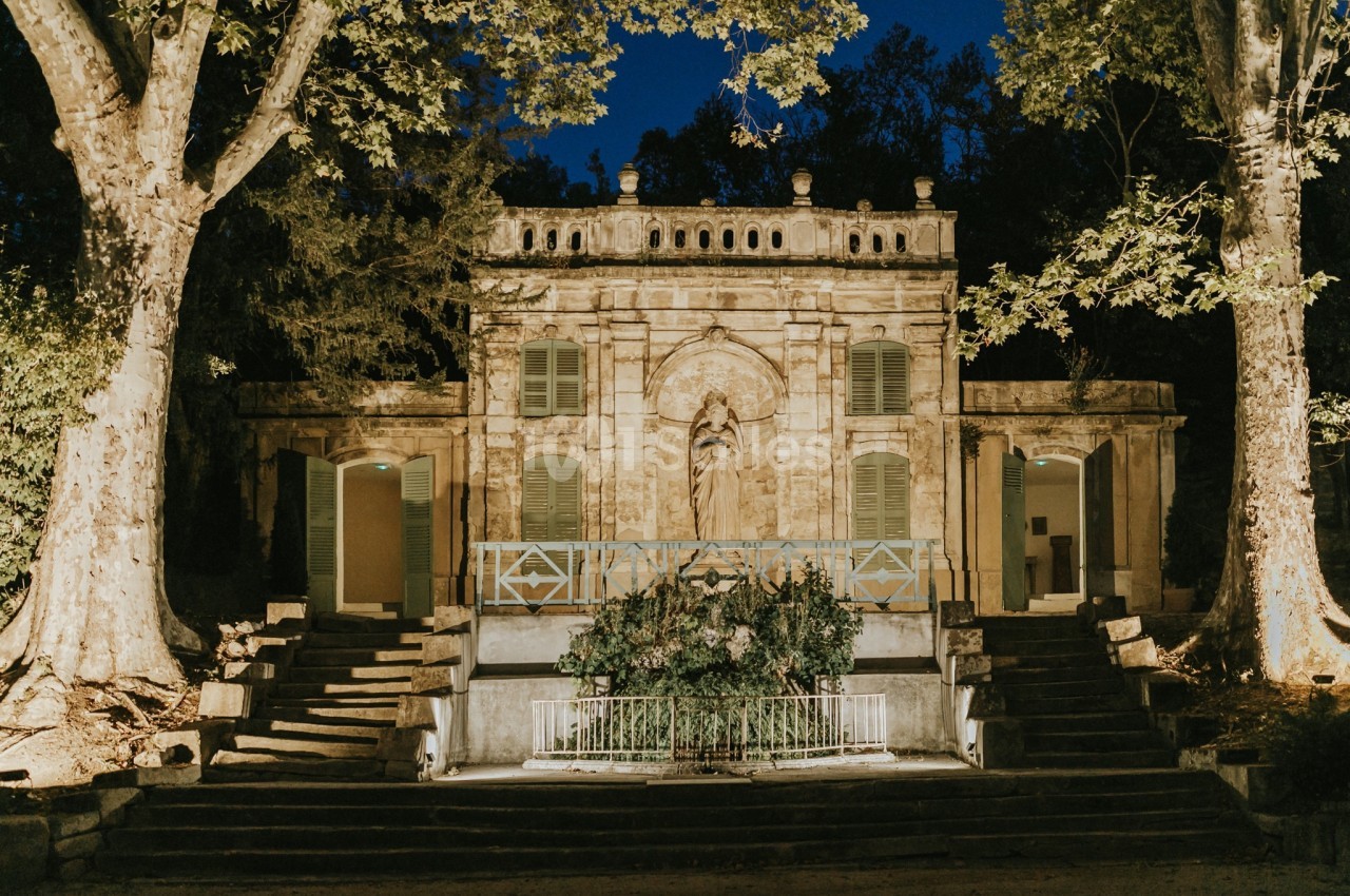 Façade d'un bâtiment ancien éclairé la nuit, entouré d'arbres et accessible par des escaliers.