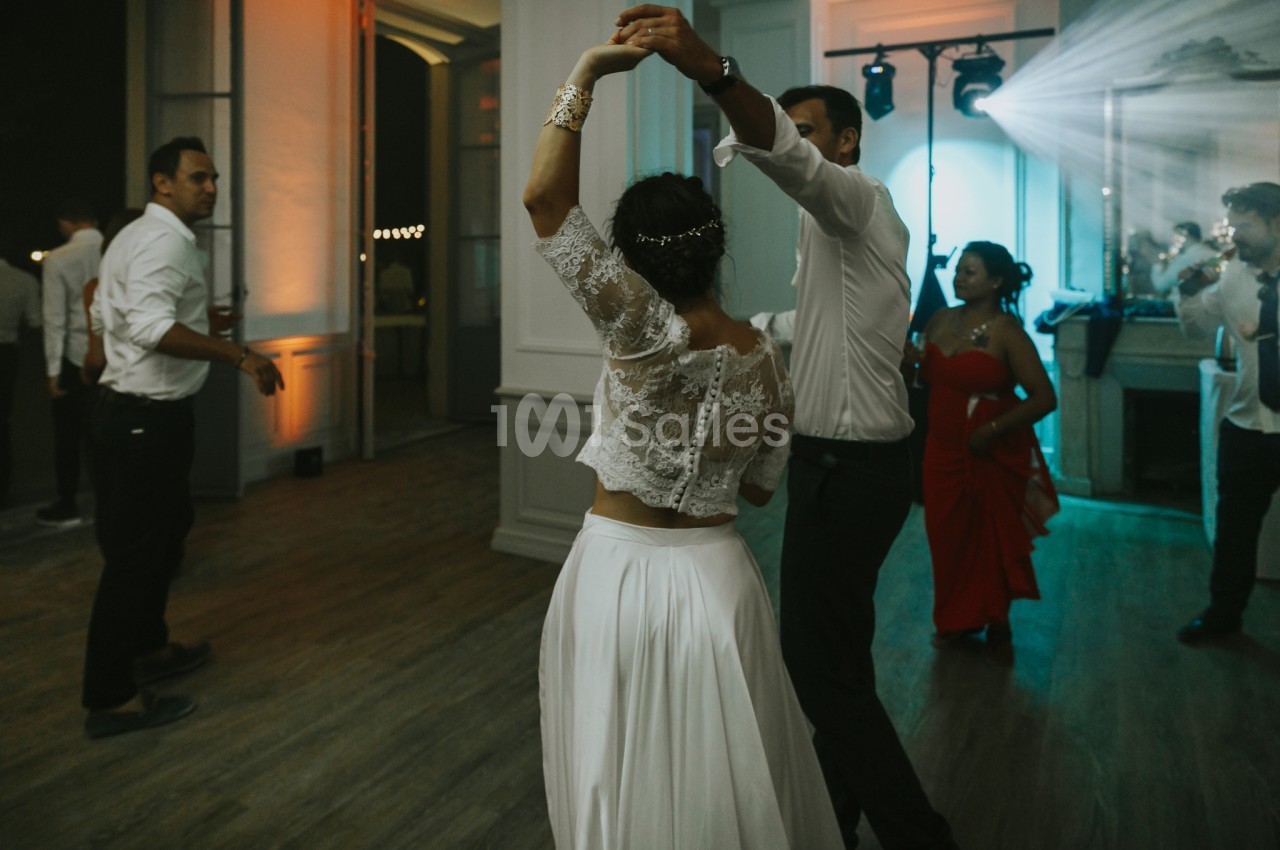Un couple danse dans une salle éclairée, entouré de quelques invités en tenue de soirée.