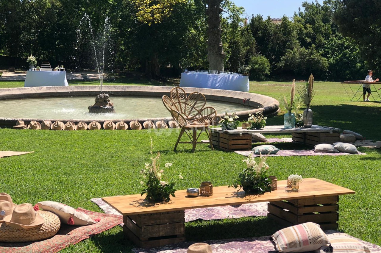 Espace extérieur aménagé avec fontaine, tables basses en bois, coussins et décorations sur une pelouse verdoyante.