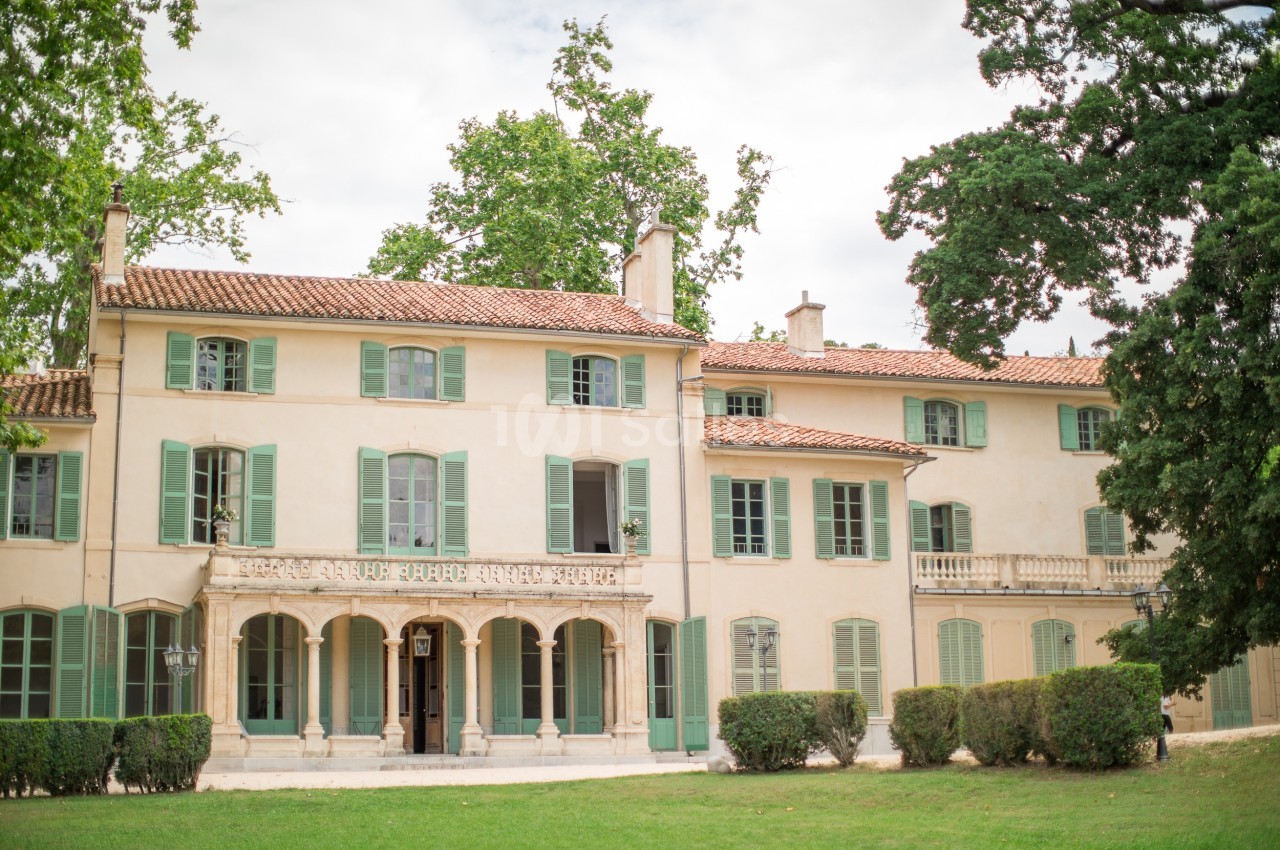 Façade d'une grande maison provençale avec volets verts, entourée d'arbres et d'un jardin.
