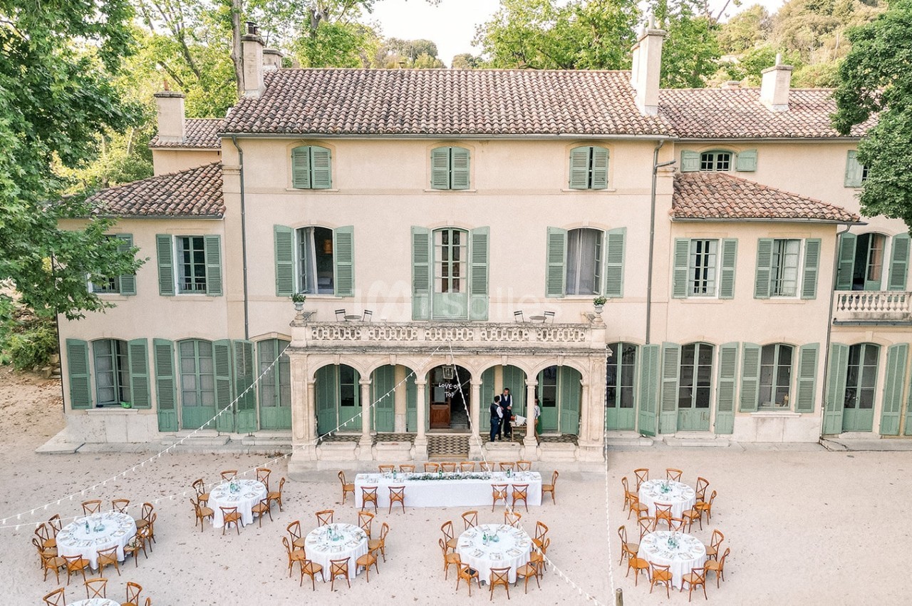 Vue aérienne d'une grande maison de style provençal avec des tables dressées pour un événement en extérieur.