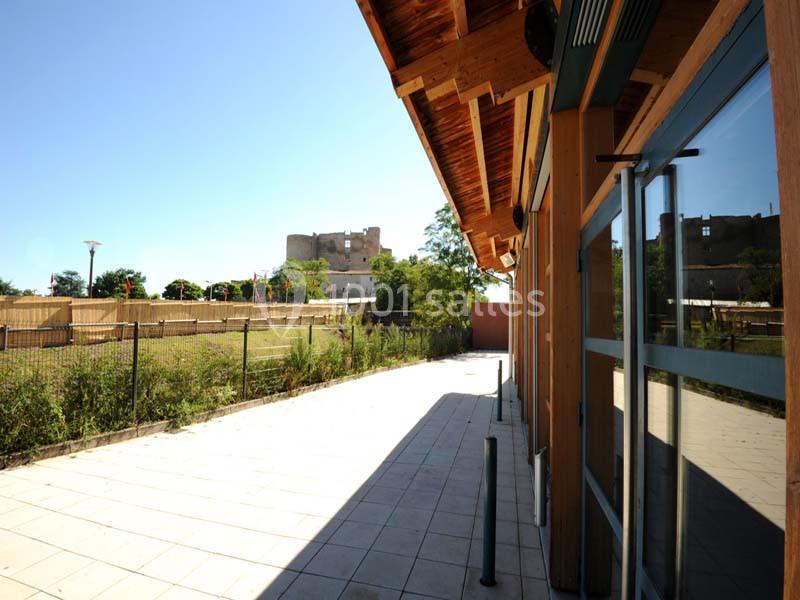 Vue d'une terrasse pavée bordée d'un bâtiment en bois, avec un château en arrière-plan sous un ciel dégagé.