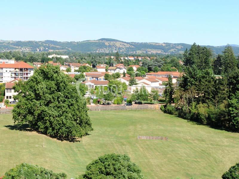 Vue d'un parc avec une grande pelouse, des arbres, des maisons en arrière-plan et des collines à l'horizon.