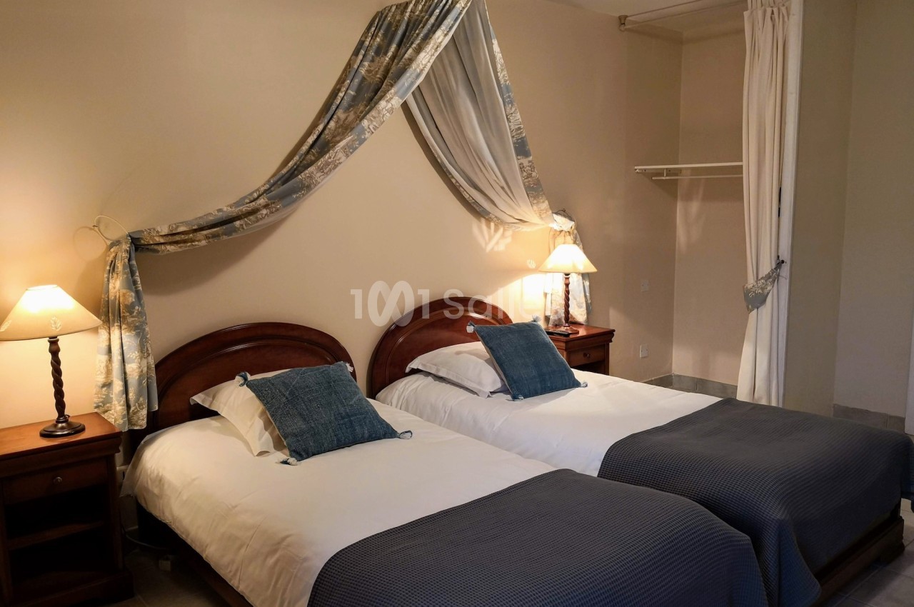 Deux lits simples avec couvre-lits bleus, encadrés par des tables de chevet et éclairés par des lampes, dans une chambre…