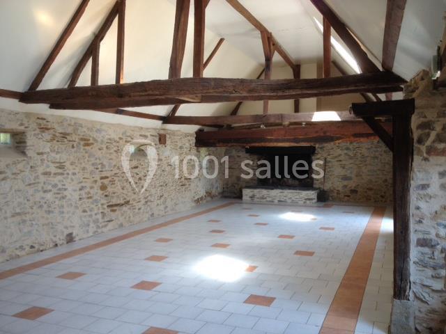 Salle lumineuse avec murs en pierre, poutres apparentes et cheminée, sol carrelé avec motifs géométriques.