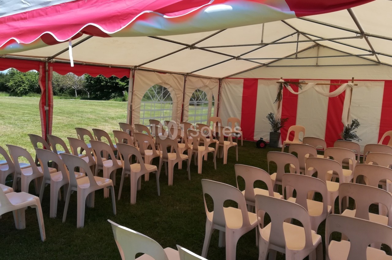Chaises en plastique disposées sous une tente blanche et rouge installée sur une pelouse.