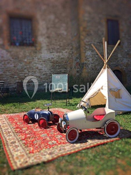 Deux voitures à pédales rétro sur un tapis rouge devant une tente tipi et un tableau noir dans un jardin.