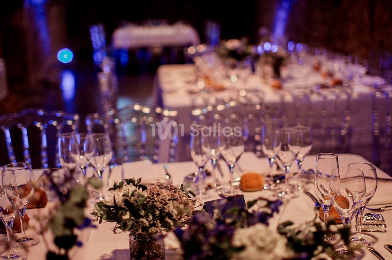 Tables décorées avec des fleurs et des verres en cristal dans une salle éclairée d'une lumière tamisée.