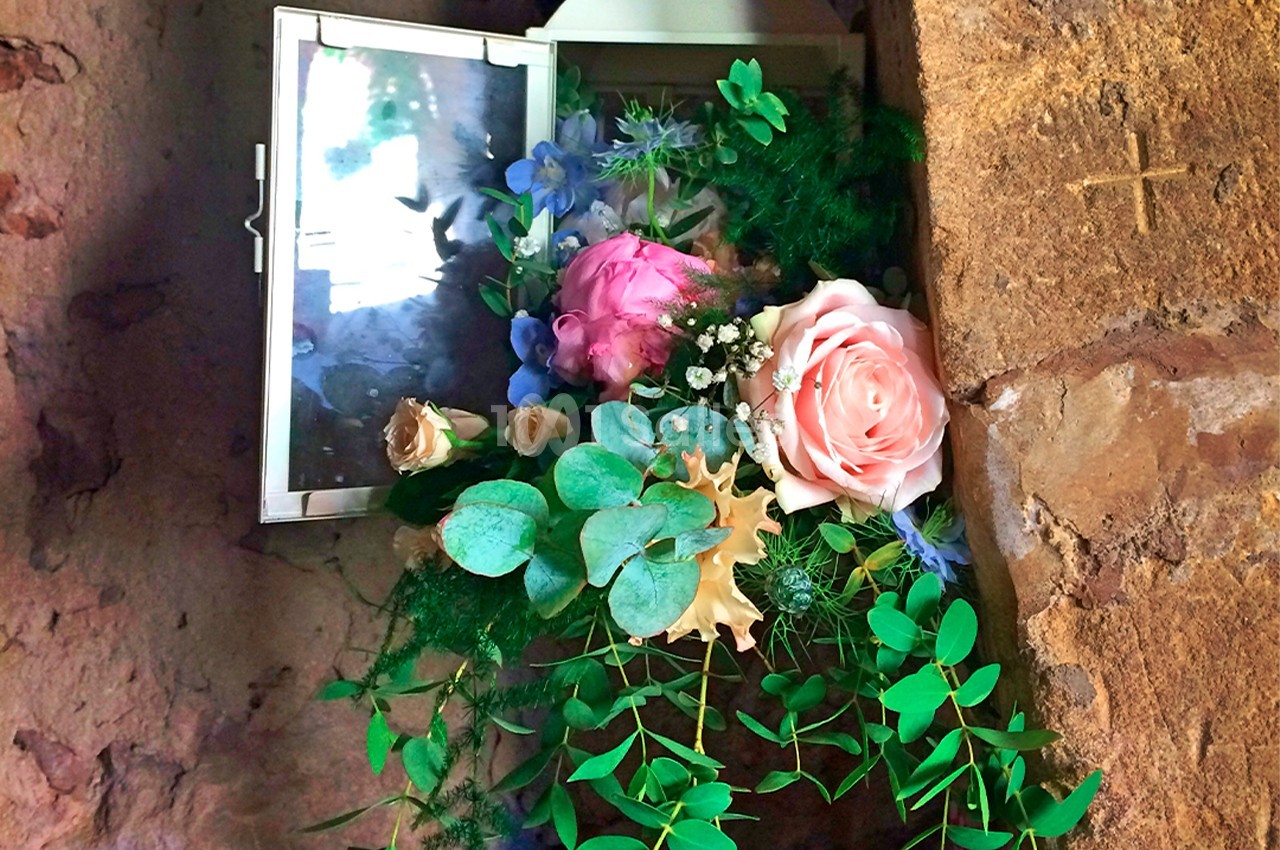 Arrangement floral avec roses, eucalyptus et feuillage, placé dans une niche murale en pierre avec une petite fenêtre…