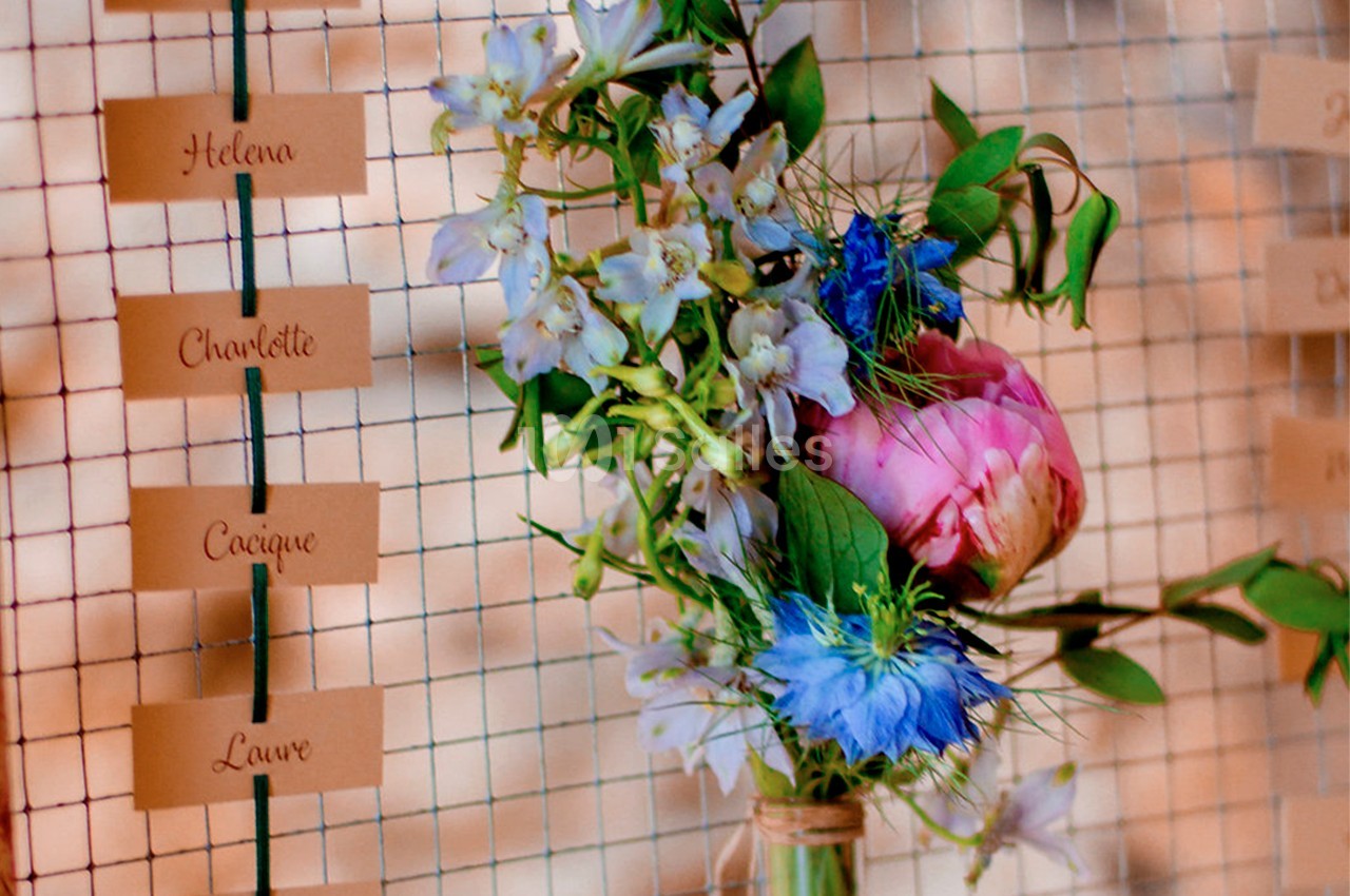 Bouquet de fleurs colorées avec des étiquettes de noms suspendues sur un fond de grille métallique.