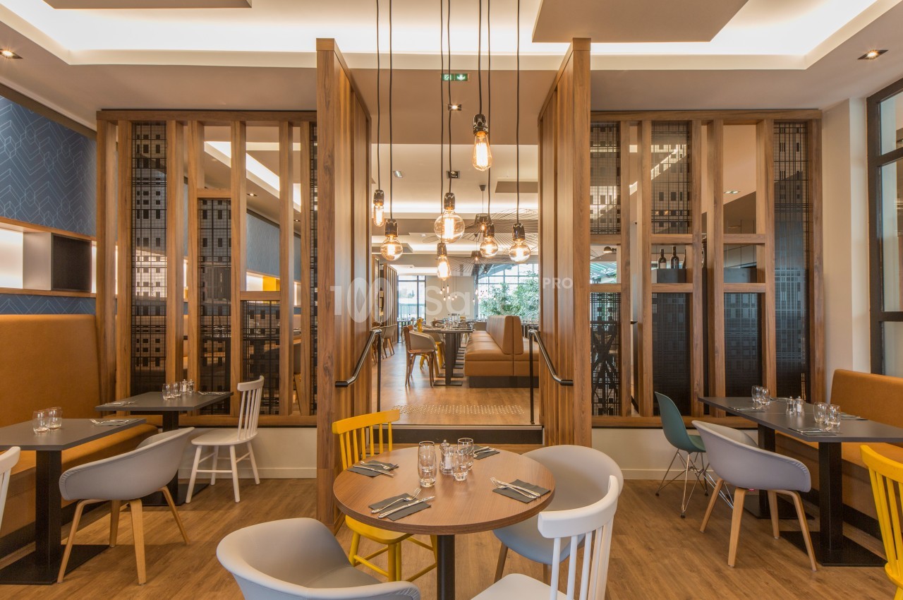 Salle de restaurant moderne avec tables en bois, chaises colorées et éclairage suspendu chaleureux.